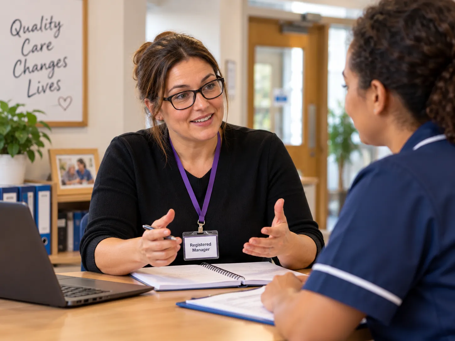 A registered manager talking through notes with a care assistant at a desk